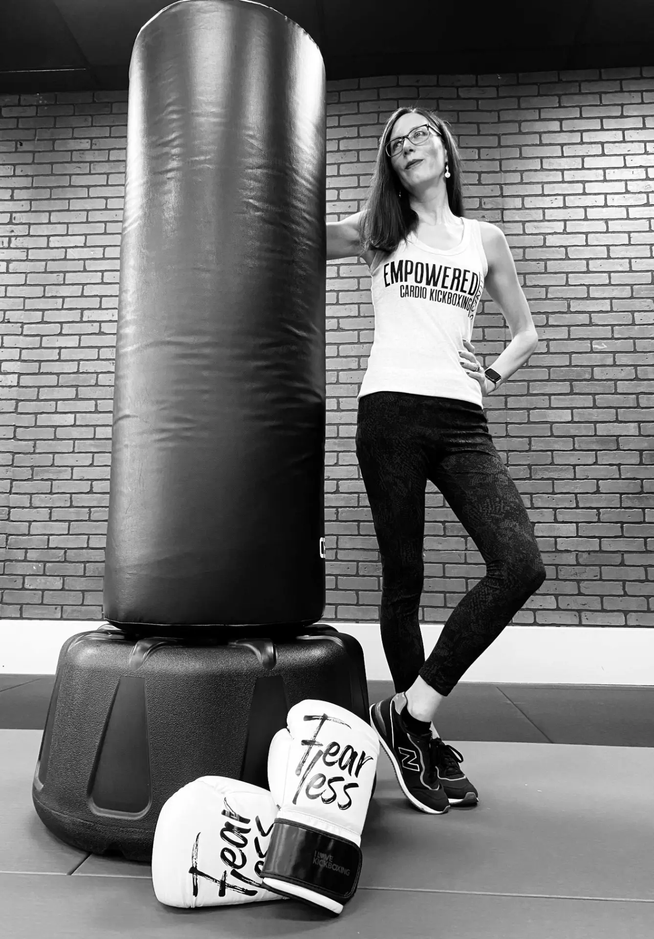 Sheena, owner and head kickboxing coach, beside a heavy bag holding Fearless boxing gloves at EMPOWERED Fitness Studio in Evansville, IN